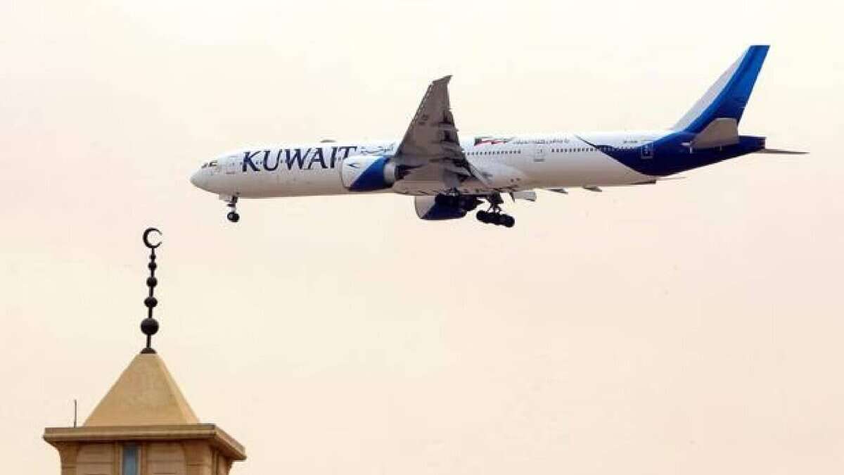 Kuwait Airways aircraft flying over mosque minaret with crescent moon symbol, approaching landing during daylight.