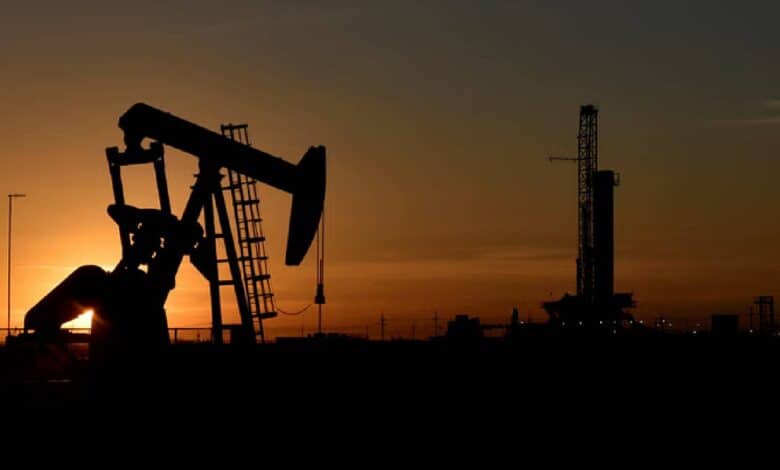Silhouette of an oil pumpjack and drilling rig at sunset in an oil field.