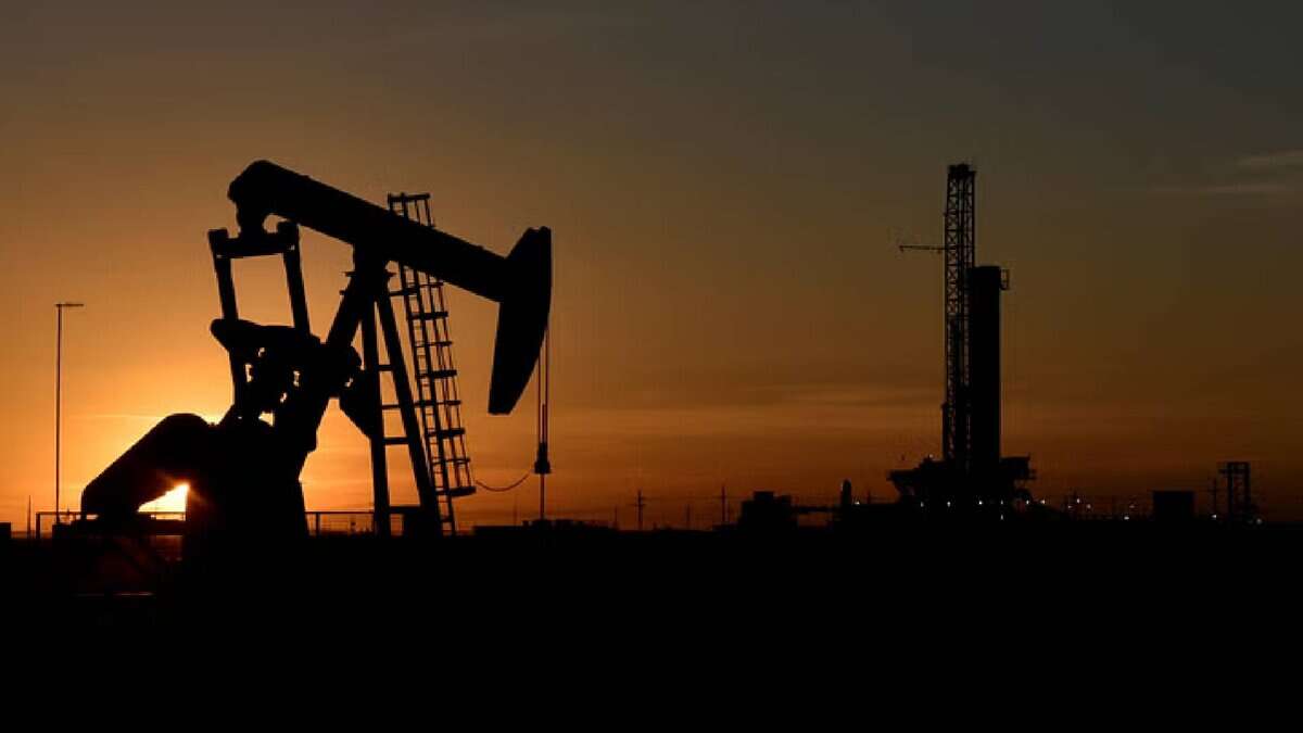 Silhouette of an oil pumpjack and drilling rig at sunset in an oil field.