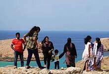 Group of people enjoying a scenic view of the Indian Ocean from a rocky hilltop in Bandar Al Khairan, Oman, with turquoise waters and rugged cliffs in the background.