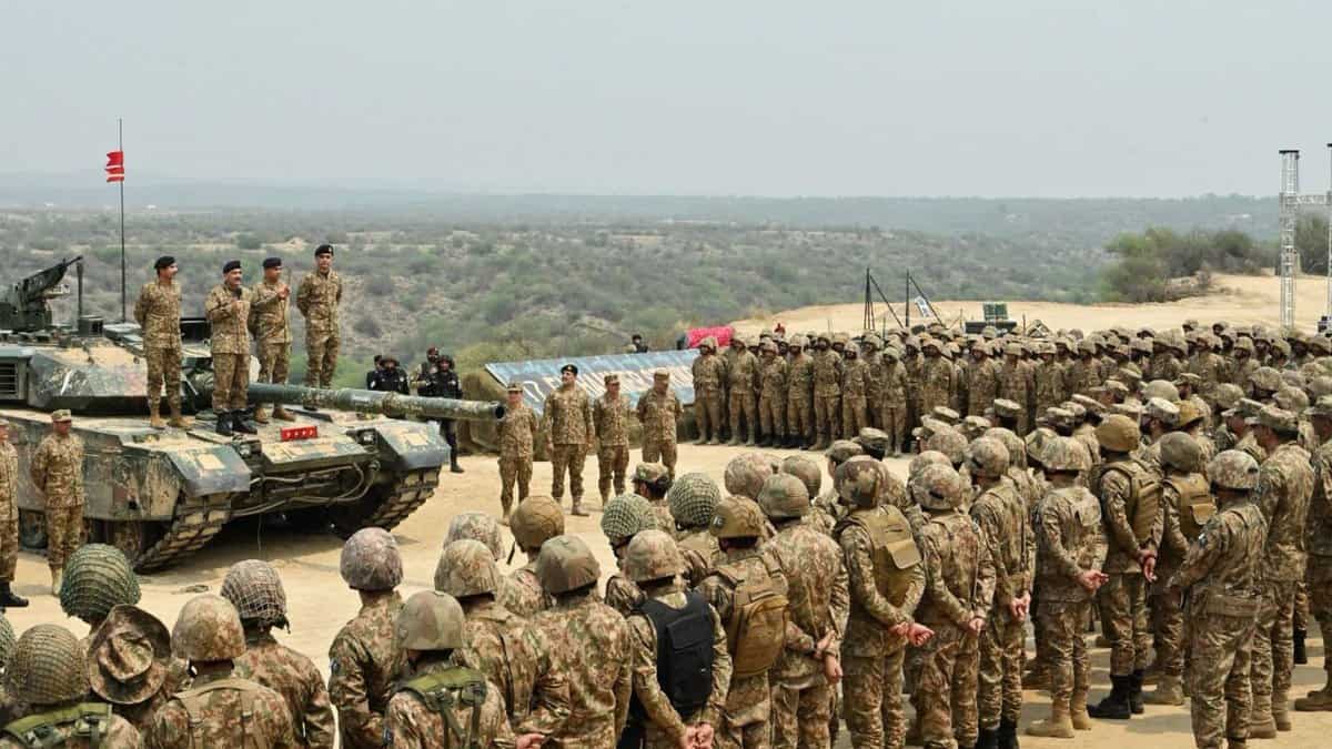 Pakistani soldiers gather around tanks during a military exercise in a desert area with senior officers.