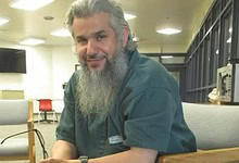 Saudi citizen Homaidan Al-Turki sitting in a detention facility, smiling slightly while holding eyeglasses.