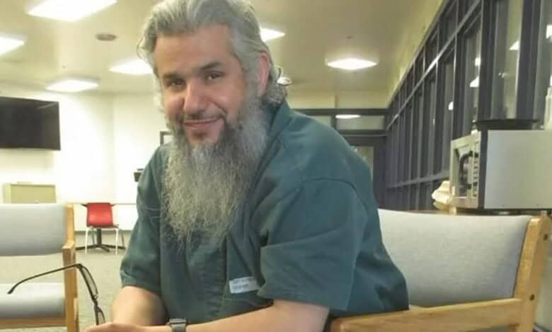 Saudi citizen Homaidan Al-Turki sitting in a detention facility, smiling slightly while holding eyeglasses.