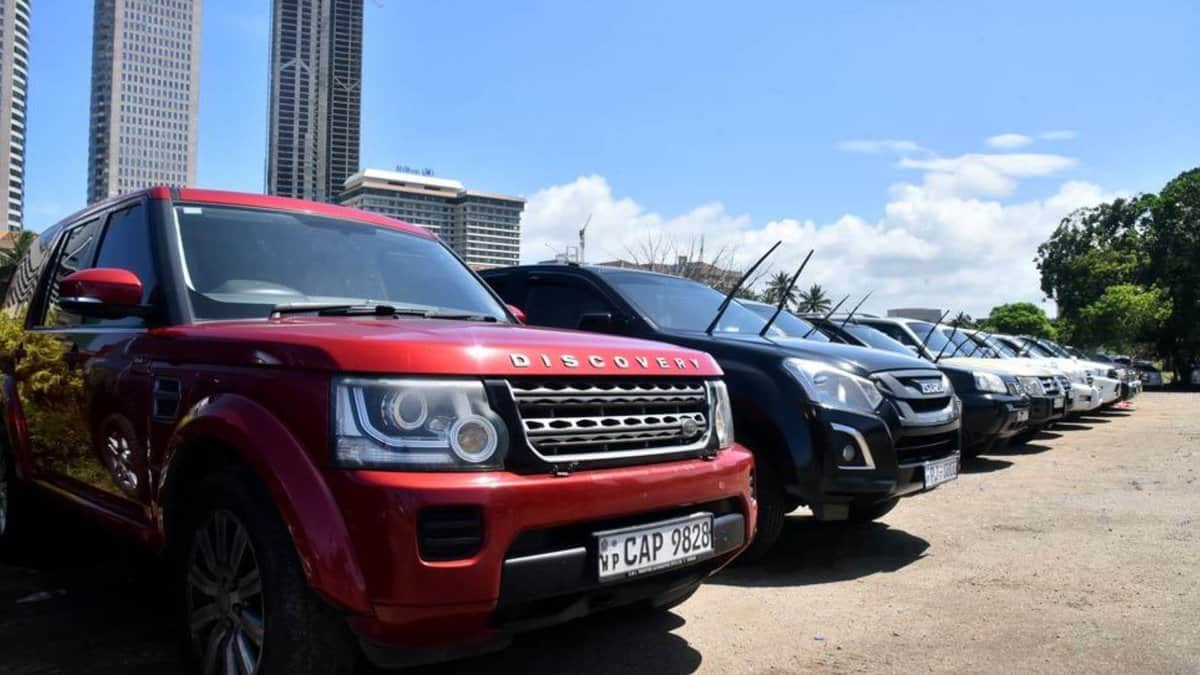 Row of parked SUVs including a red Land Rover Discovery, with tall city buildings and a clear blue sky in the background.
