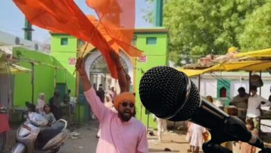 The image displays a man with a saffron turban waving a saffron flag in the background and a mike in the forground