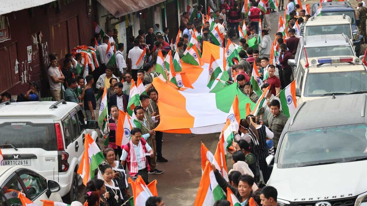 The image displays a picture of scores of people holding the national flag as part of the Tiranga Yatra