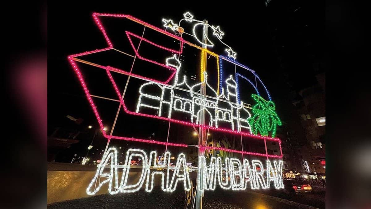 Eid Al Adha light decoration with mosque, crescent moon, and Adha Mubarak message in vibrant colours at night.