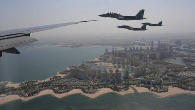 Qatar Emiri Air Force F-15 fighter jets escort Air Force One over The Pearl in Doha, Qatar, with the city's coastal skyline visible below on a clear day.