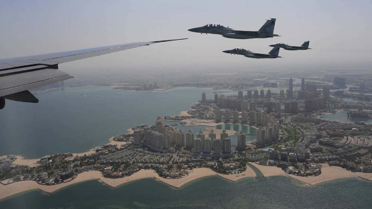 Qatar Emiri Air Force F-15 fighter jets escort Air Force One over The Pearl in Doha, Qatar, with the city's coastal skyline visible below on a clear day.