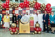 Officials and staff pose with balloons and signage celebrating the 500th winner of the Dubai Duty Free Millennium Millionaire draw at Dubai Airport, with a draw drum at the centre of the event.