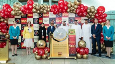 Officials and staff pose with balloons and signage celebrating the 500th winner of the Dubai Duty Free Millennium Millionaire draw at Dubai Airport, with a draw drum at the centre of the event.