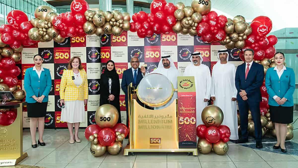 Officials and staff pose with balloons and signage celebrating the 500th winner of the Dubai Duty Free Millennium Millionaire draw at Dubai Airport, with a draw drum at the centre of the event.