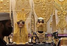 A man walks past a Dubai gold shop showcasing extravagant gold jewellery sets, including full-body ornaments, necklaces, and headpieces displayed on mannequins.