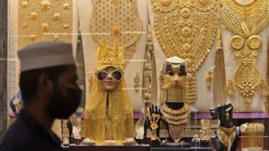 A man walks past a Dubai gold shop showcasing extravagant gold jewellery sets, including full-body ornaments, necklaces, and headpieces displayed on mannequins.