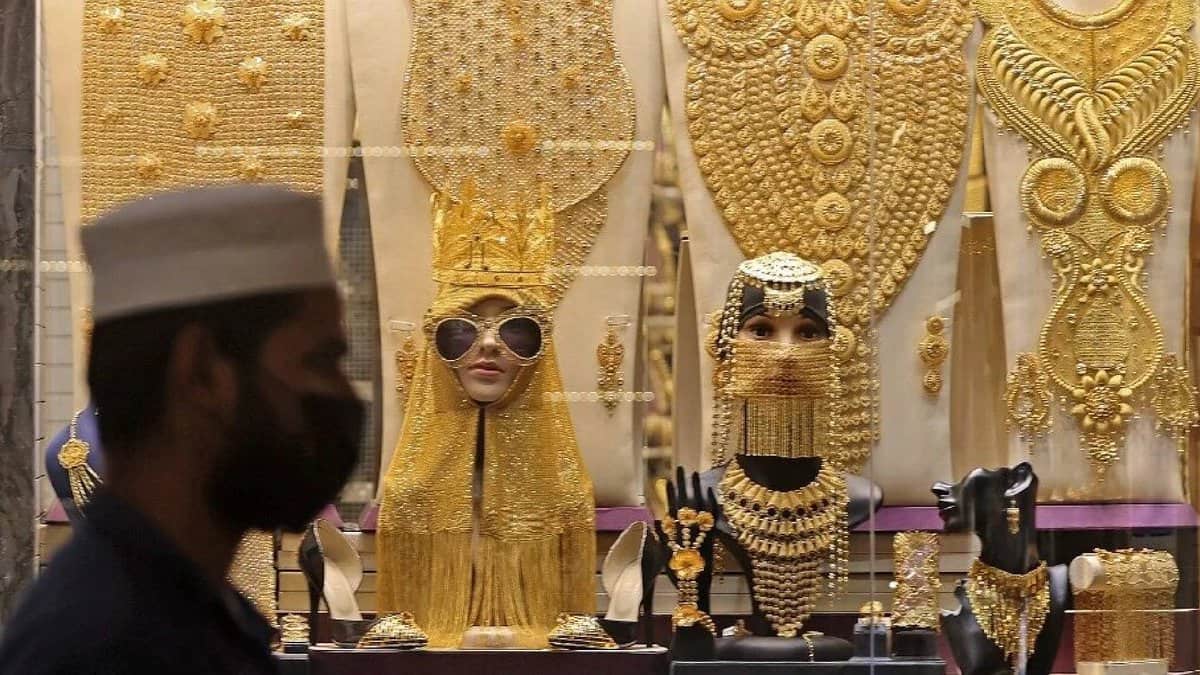 A man walks past a Dubai gold shop showcasing extravagant gold jewellery sets, including full-body ornaments, necklaces, and headpieces displayed on mannequins.