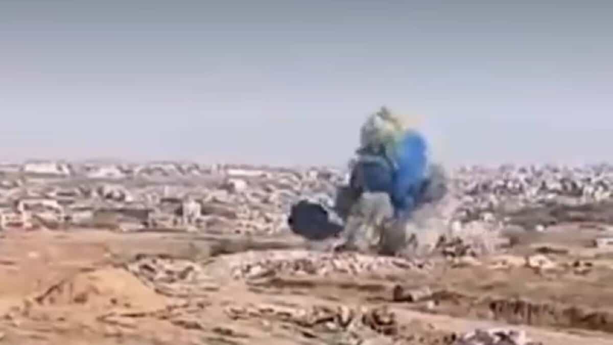Explosion in Gaza releasing blue smoke, allegedly part of a gender reveal by Israeli soldiers, with urban ruins visible in the background.