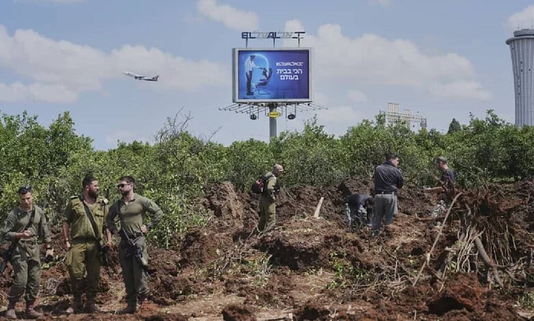 Israeli security forces inspect impact site of Houthi missile near Ben Gurion Airport, with visible damage and airport control tower in the background.
