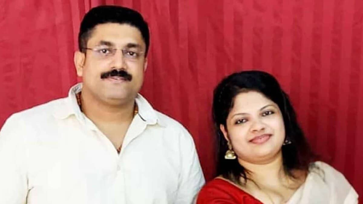Suraj and Binsi, an Indian couple from Kerala, smiling together in a posed photo against a red curtain backdrop.