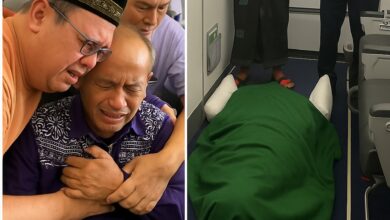 A grieving Indonesian man is consoled aboard a Saudi Arabian Airlines flight after his wife, a Haj pilgrim, died unexpectedly en route to Madinah. The deceased is respectfully covered in a green cloth and laid on the aircraft floor near the exit. Two men, including one in official uniform, stand in mourning. 