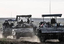 Israeli army tanks and armoured vehicles advancing through a dusty field near Gaza border during a military operation.