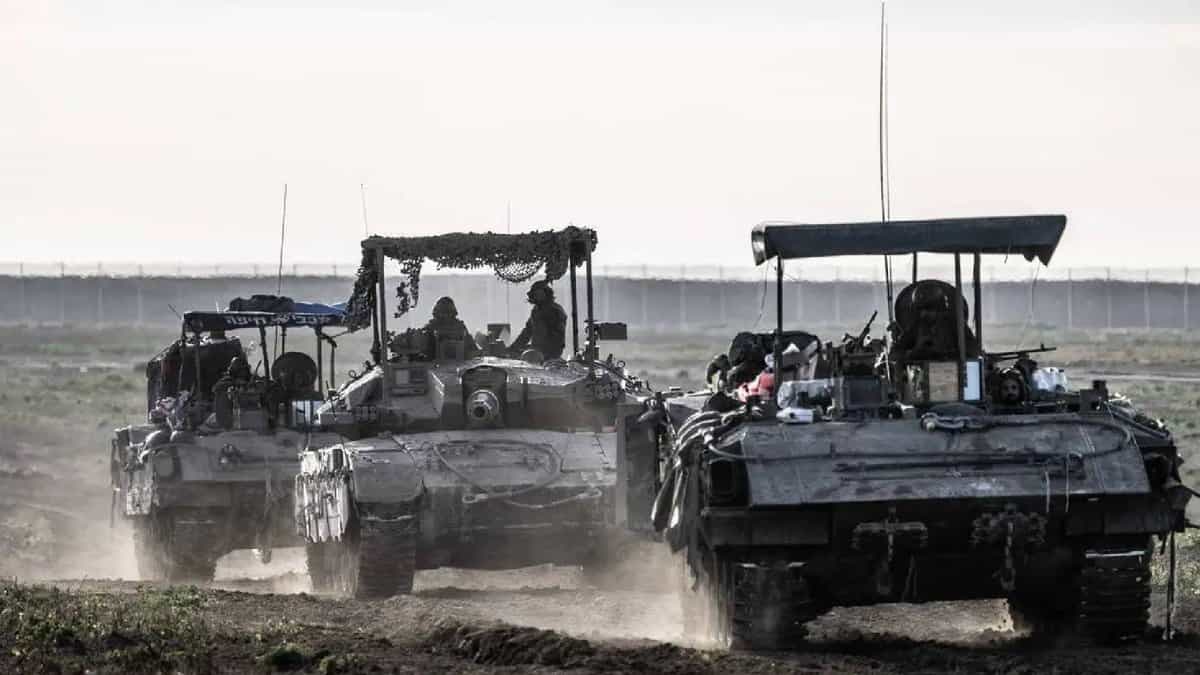 Israeli army tanks and armoured vehicles advancing through a dusty field near Gaza border during a military operation.