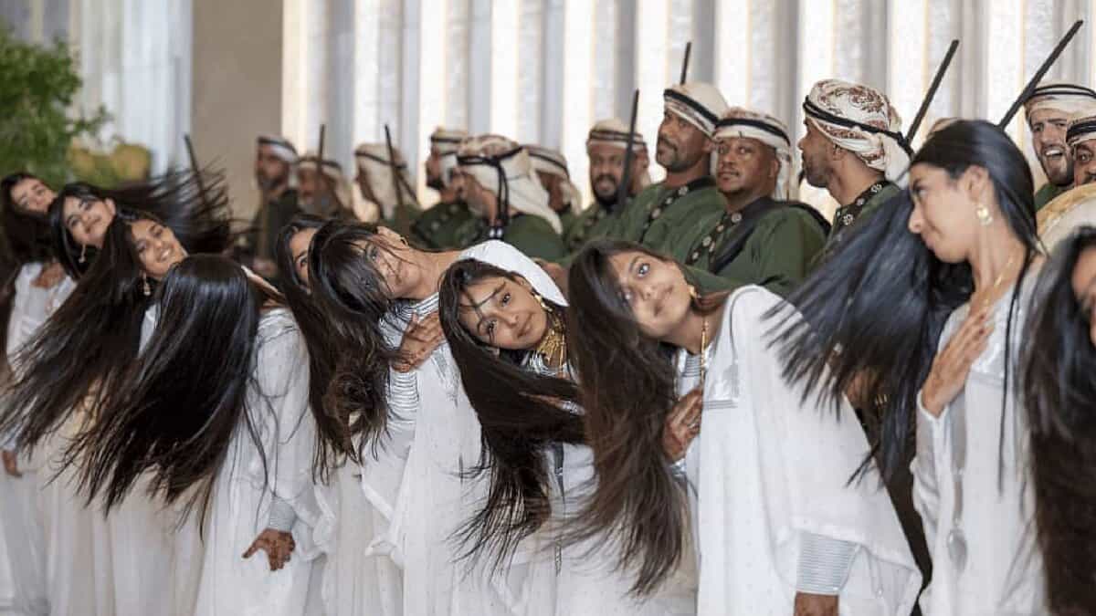 Emirati girls in white gowns perform the traditional Khaleeji dance by rhythmically flipping their hair in unison, as part of a ceremonial welcome for U.S. President Donald Trump in Abu Dhabi. Men in traditional dress stand behind them holding swords.