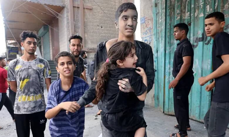 Dust-covered Palestinian children in Gaza walk through a bombed street after an Israeli airstrike, one carrying a terrified young girl to safety.