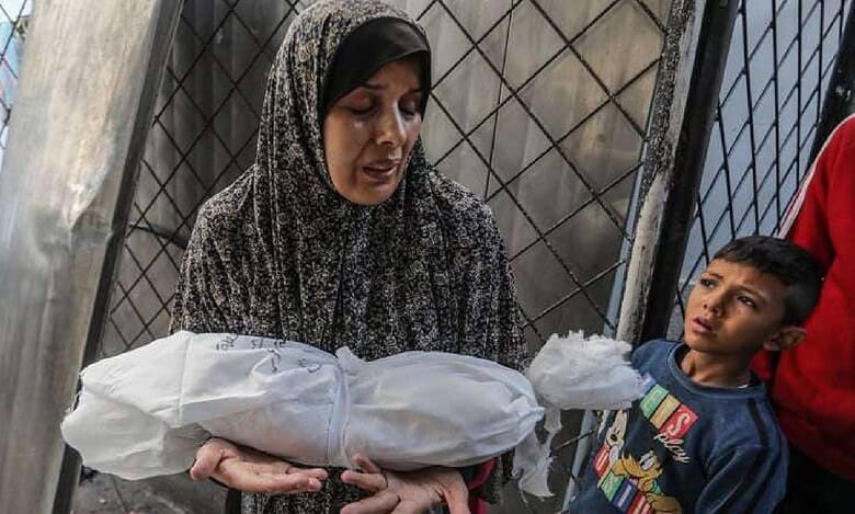 Grieving Palestinian mother holds her infant wrapped in a white shroud after Israeli airstrikes on Khan Younis, Gaza, as a young boy looks on in sorrow.