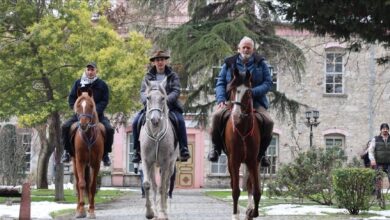 Three Spanish pilgrims on horseback during their journey to Haj. riding through a tree-lined path near a historic building.