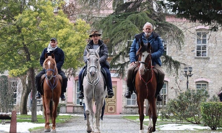 Three Spanish pilgrims on horseback during their journey to Haj. riding through a tree-lined path near a historic building.
