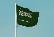 Saudi Arabian national flag waving on a clear blue sky background.
