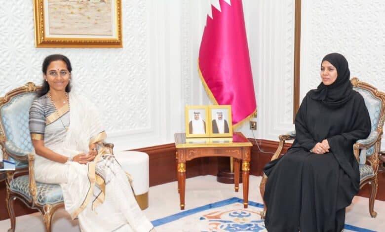 Supriya Sule, wearing a white saree, seated with Dr Hamda Al Sulaiti in a formal meeting room with the Qatar flag and portraits in the background.