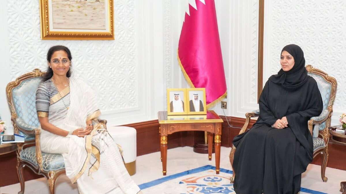 Supriya Sule, wearing a white saree, seated with Dr Hamda Al Sulaiti in a formal meeting room with the Qatar flag and portraits in the background.