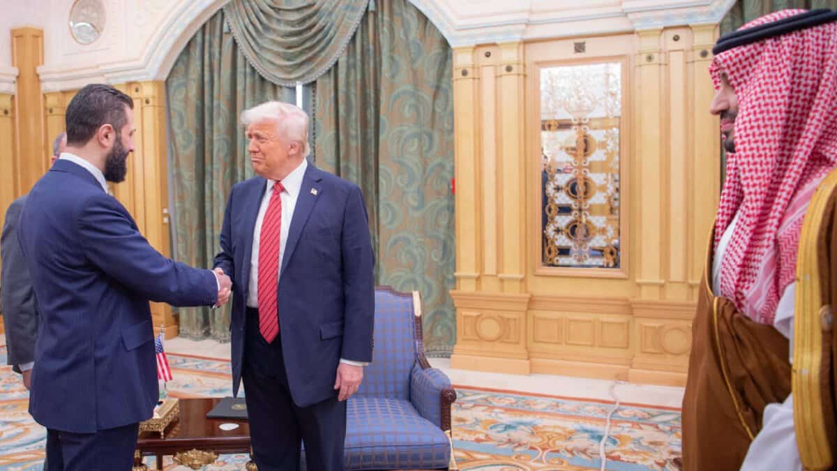 US President Donald Trump shakes hands with the interim Syrian President during a formal meeting in Saudi Arabia, as a Saudi Crown Prince observes from the side.