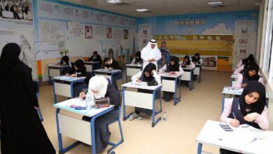 Female students in a UAE classroom take an exam under supervision, with educational posters on the walls.