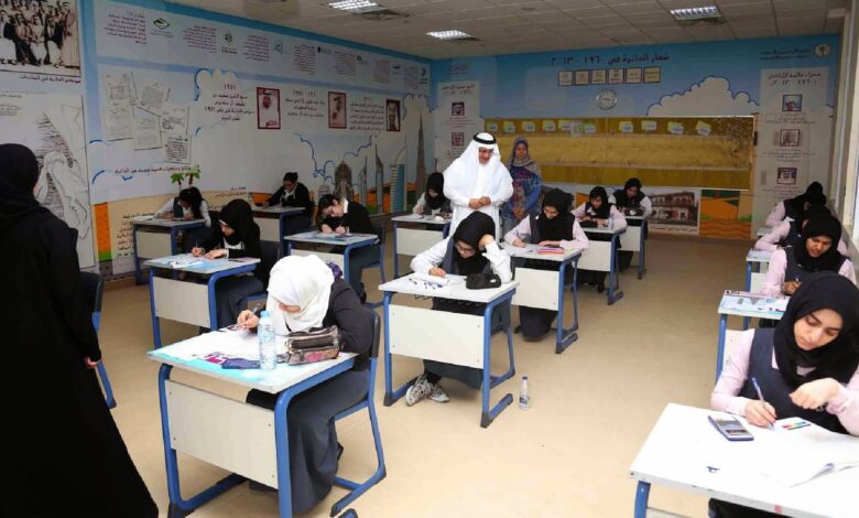 Female students in a UAE classroom take an exam under supervision, with educational posters on the walls.
