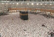 Thousands of Muslim pilgrims performing Umrah around the Kaaba at the Grand Mosque in Makkah, Saudi Arabia, during the night under bright lights and towering hotel buildings.