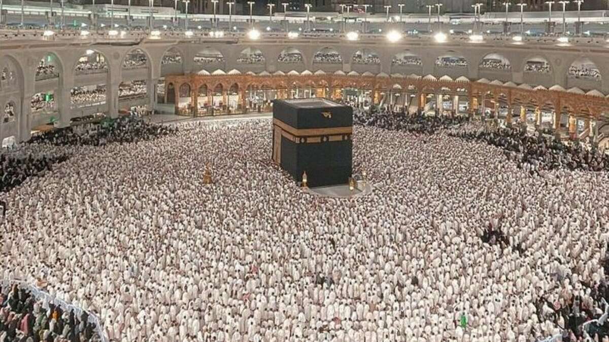 Thousands of Muslim pilgrims performing Umrah around the Kaaba at the Grand Mosque in Makkah, Saudi Arabia, during the night under bright lights and towering hotel buildings.