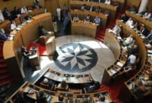 Members of the Corsican Assembly seated in a circular chamber during a formal session, with documents and microphones on desks.