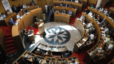 Members of the Corsican Assembly seated in a circular chamber during a formal session, with documents and microphones on desks.