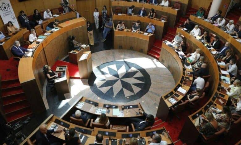 Members of the Corsican Assembly seated in a circular chamber during a formal session, with documents and microphones on desks.