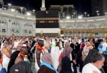 A large gathering of international pilgrims dressed in white Ihram and traditional attire at Makkah’s Grand Mosque, with the Kaaba in the background, during the night ahead of Haj 2025.