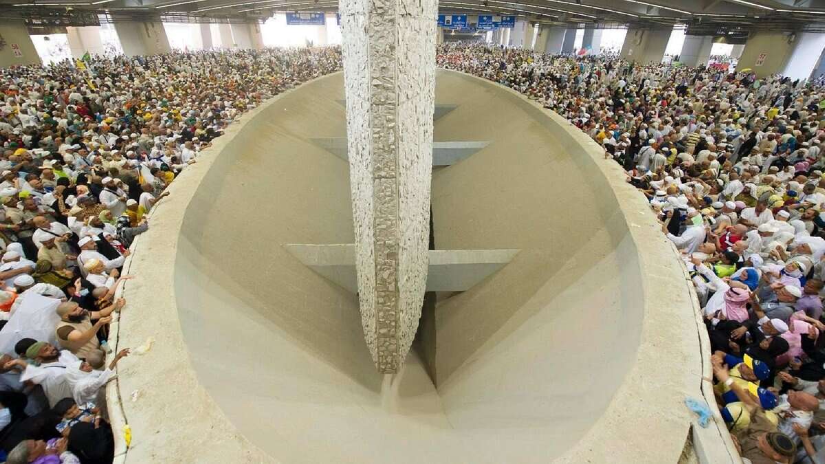A large crowd of Haj pilgrims gathers around the Jamarat pillars in a spacious indoor area, performing the ritual of stoning the devil on June 6, 2025.