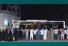 The image displays a group of 53 expatriates stands in front of a bus at night in Makkah, Saudi Arabia, after being arrested by Haj Security Forces for attempting to perform Haj without a permit on June 5.