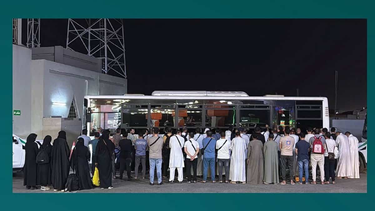 The image displays a group of 53 expatriates stands in front of a bus at night in Makkah, Saudi Arabia, after being arrested by Haj Security Forces for attempting to perform Haj without a permit on June 5.