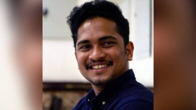 The image of 29-year-old Issac Paul Olakkengil, smiling and wearing a dark blue shirt, seated indoors.