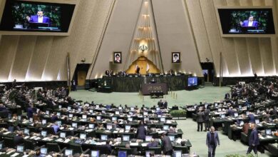 The image of a Iranian parliamentary chamber with lawmakers at computer desks, central podium with emblem and portraits, and screens showing a speaker, under a triangular ceiling, June 25, 2025.