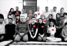 The image of a black-and-white group photo of 12 people, including men, women, and children, sitting and standing on a patterned rug, with red heart symbols overlaid on each person, symbolising their loss in a tragic airstrike.