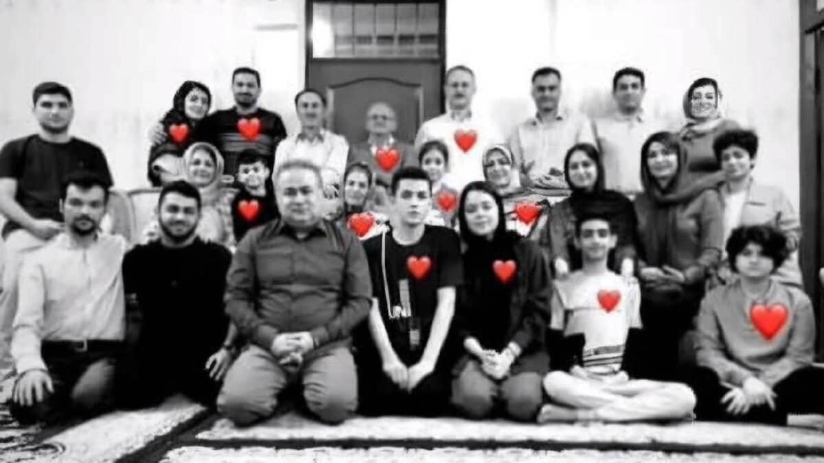 The image of a black-and-white group photo of 12 people, including men, women, and children, sitting and standing on a patterned rug, with red heart symbols overlaid on each person, symbolising their loss in a tragic airstrike.