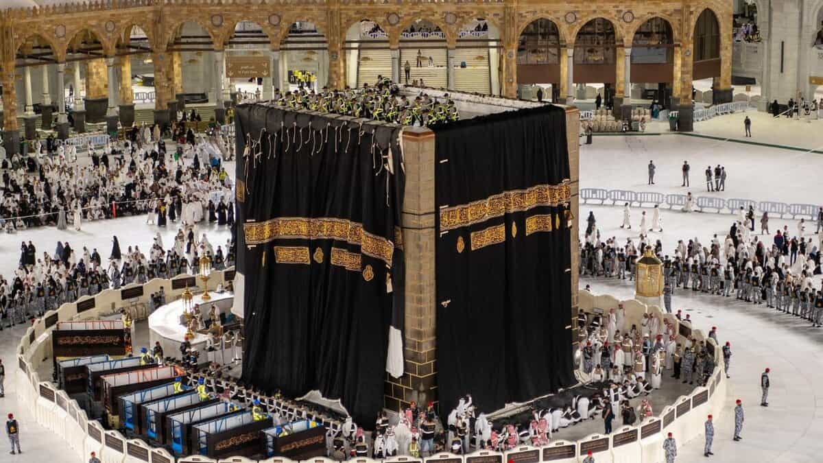 Workers replace the Kiswah (cloth covering) of the Kaaba at the Grand Mosque in Makkah, surrounded by pilgrims and security personnel.